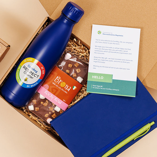 Box containing a blue bottle, snacks, and a card on a beige background