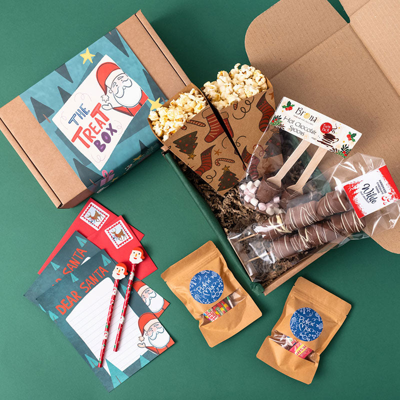 A kraft gift box filled with treats including a popcorn holder with red socks, Keogh's popcorn, a chocolate bar with a red wrapper, a Christmas colouring book, hot chocolate and a 'Dear Santa' letter.
