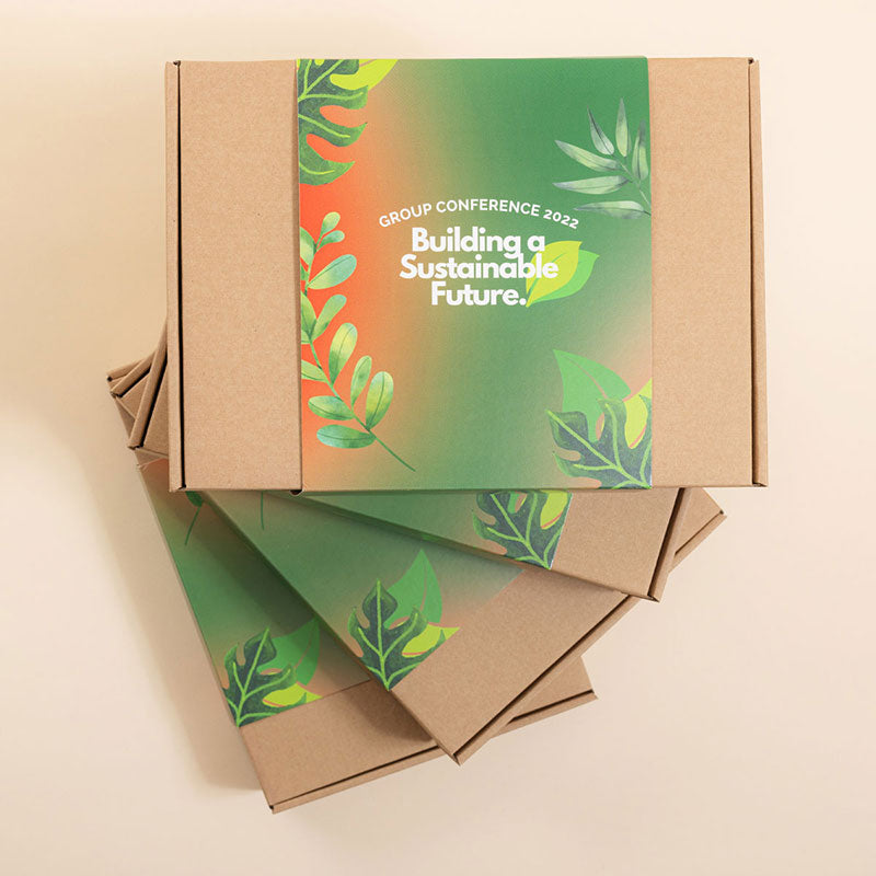 Beige background with four kraft gift boxes on the right hand side with a green and red sleeve wrapped around the box. The text reads 'Building a Sustainable Future'.